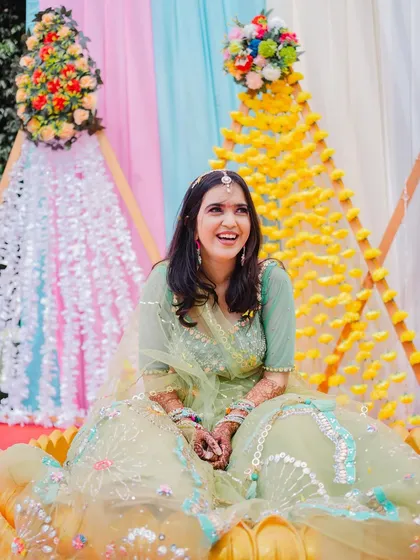 A radiant, smiling portrait of the bride during her Haldi ceremony, surrounded by beautiful floral decorations.