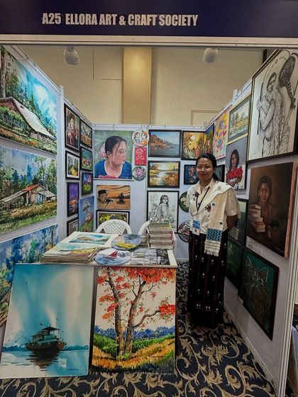A visitor posing at my exhibition booth, which is filled with my landscape paintings and portraits.