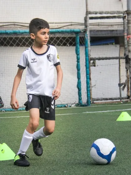 Focused and determined, a young athlete practices dribbling through cones, a fundamental part of our youth soccer training curriculum.