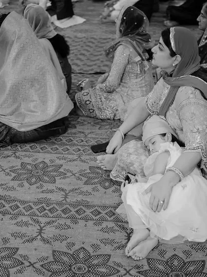 A touching black and white photo of a young child asleep in her mother's lap during a ceremony. This quiet, candid moment beautifully illustrates the peaceful trust between a mother and child.