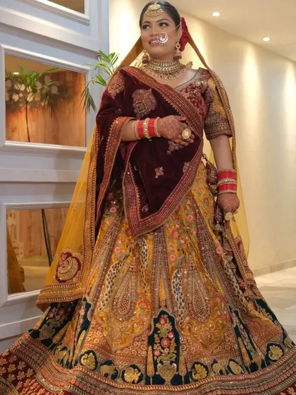 A full-length view of a bride in our multi-panel velvet lehenga. The combination of deep maroon, mustard yellow, and dark teal panels creates a unique and regal bridal outfit.