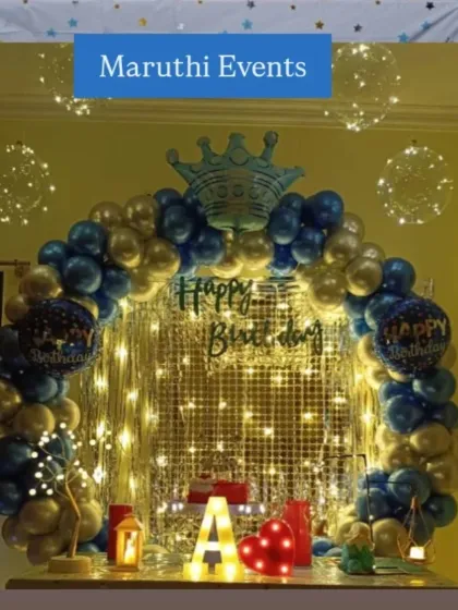 A royal-themed birthday table decoration with a blue and gold balloon arch, a crown, and fairy lights for a magical touch.
