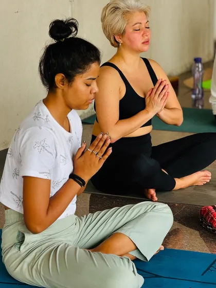 Two students sit in prayer pose, their eyes closed in meditation. This practice helps to bring balance to the body and mind.