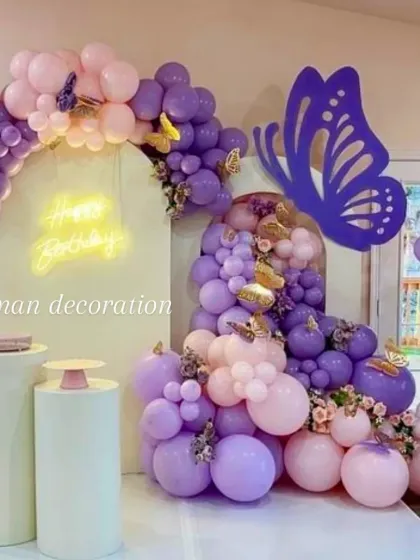 A detailed shot of the butterfly-themed balloon cascade, showing the mix of purple and pink balloons with small gold butterfly accents.