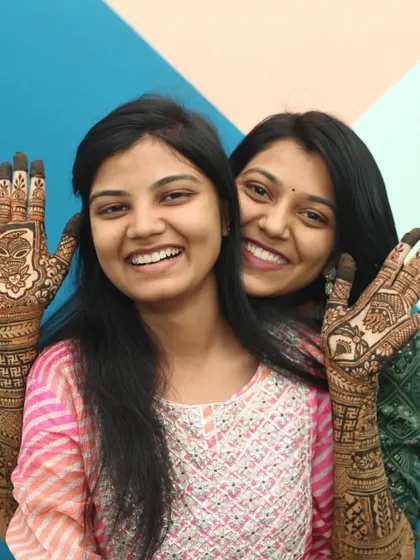 Sisters sharing a laugh during the Mehandi ceremony, showing off their intricate henna designs. Our candid wedding photography aims to capture the genuine bonds and happy interactions between family and friends.
