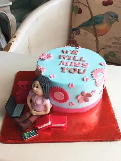 A sweet farewell cake with a "We Will Miss You" message, decorated with a personalized figure and items representing her hobbies.