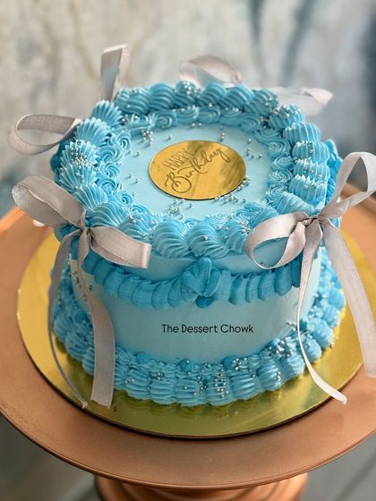 This custom tall cake in blue features a vintage Lambeth piping style with delicate ribbon details. It's a sophisticated design for a birthday celebration.