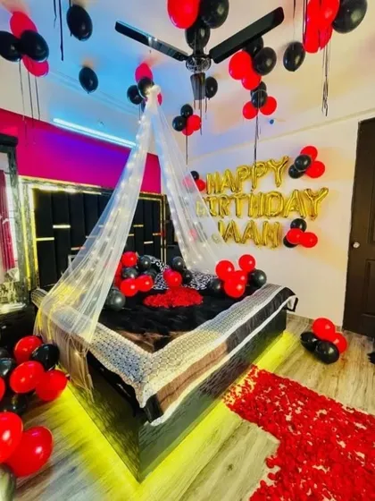 A bold and romantic birthday room decoration for 'Jaan'. The black and red theme, fairy light canopy, and rose petal path create a dramatic and passionate atmosphere.