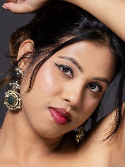 A close-up beauty portrait focusing on a pair of ornate, vintage-style earrings. The model's expression is soft, drawing attention to the accessories.