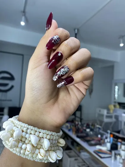 A bold and glamorous bridal option with coffin-shaped nails. This set pairs a deep maroon base with accent nails completely covered in chunky silver glitter and stones.