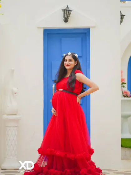 A graceful solo portrait of the mother-to-be in a vibrant red gown against a clean, modern backdrop.