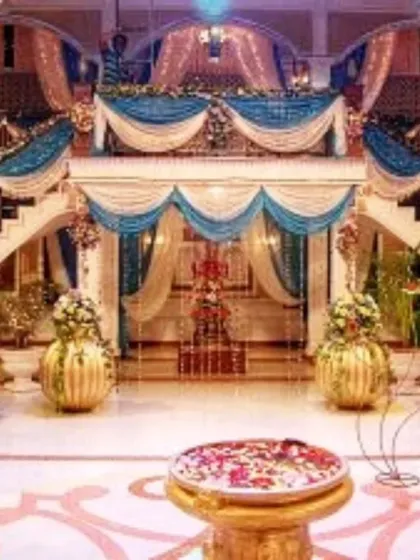 A palatial indoor wedding decoration, using the venue's grand staircase as part of the decor with blue and gold drapes and large floral vases.