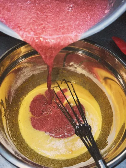 Pouring the raspberry puree into the egg mixture. The vibrant color comes entirely from the fruit itself.