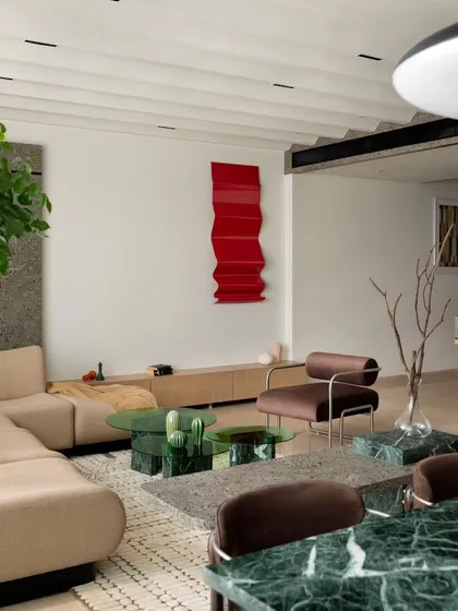 The bold red metal art piece in the living room is a nod to the client's family roots in the metal industry. It provides a vibrant contrast to the neutral and green tones of the surrounding space.