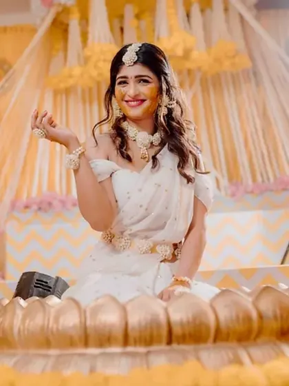 The bride looking stunning in her white saree against the vibrant yellow decor of her Haldi ceremony.