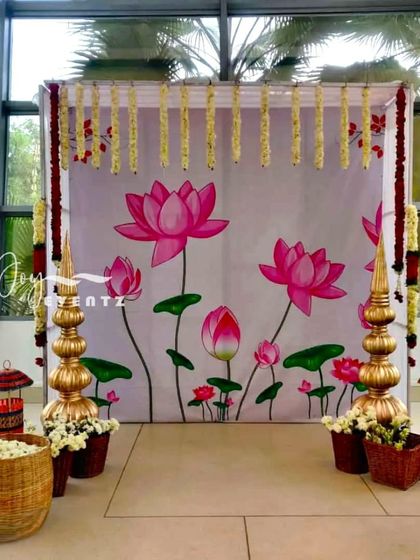 This photo booth setup for a half saree function features a hand-painted lotus backdrop. We framed the setup with jasmine garlands and placed traditional brass and wicker props in the foreground.