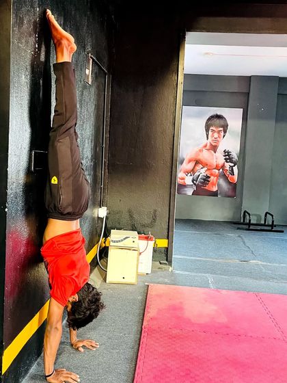 A student holds a handstand against the wall, building shoulder strength and balance.