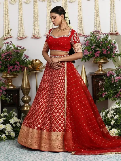A quintessential bridal look, this red silk lehenga features intricate golden embroidery and a traditional silhouette. The matching embellished blouse and net dupatta create a look of timeless elegance.