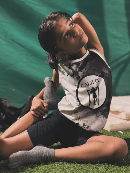 This young athlete shows impressive flexibility in a deep stretching pose, wearing her Califit pride on her shirt.