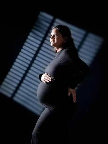 A side profile using the same dramatic lighting technique. This pose beautifully highlights the shape of the baby bump while maintaining an artistic and moody feel.
