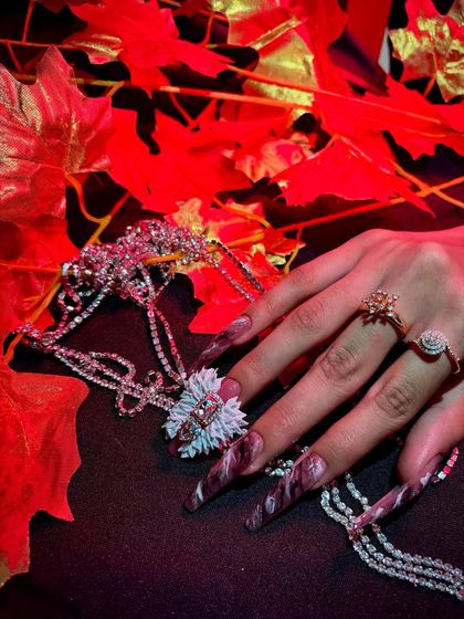 A dramatic and moody shot of long, stiletto nails with a marble effect and a large 3D flower.