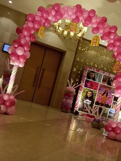 A pink balloon arch and photo collage backdrop creating a personalized entrance for a Barbie-themed party.