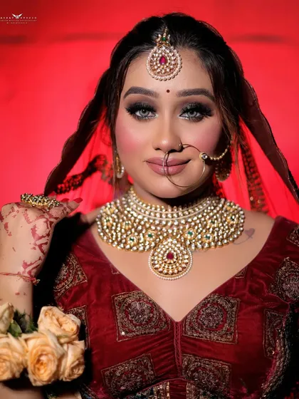 A classic bridal portrait with a direct gaze, capturing the complete makeup and jewelry look against a vibrant red background.
