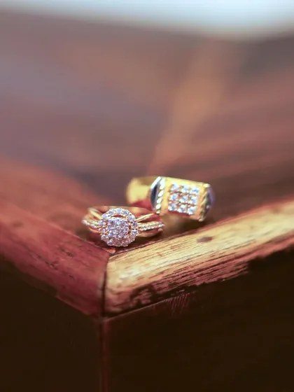 A detailed close-up of the bride and groom's engagement rings resting on a wooden surface. This macro shot highlights the beautiful design and sparkle of the rings that mark their commitment.