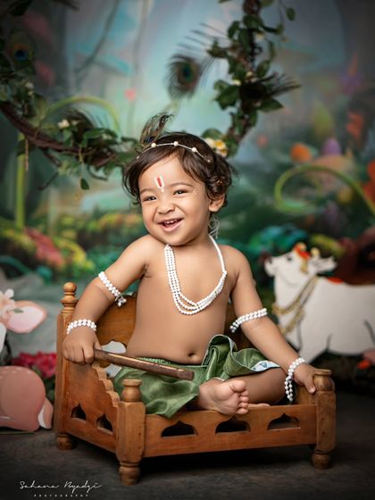 A happy little Krishna, sitting on a tiny bed in his magical forest.