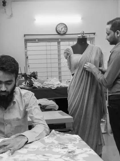 In my studio, a design takes shape. Here, I am draping fabric on a mannequin while an artisan works at a sewing machine, a glimpse into our collaborative creation process.