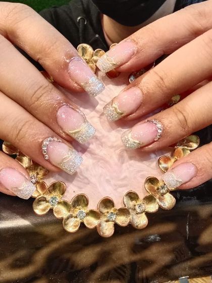 A shimmering set of square-tipped nails with a silver and gold glitter French tip design.