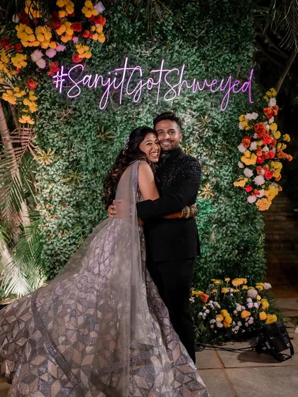 A happy hug in front of their custom wedding hashtag. The couple looks so in love, and her glamorous Sangeet look is perfect for the celebration.
