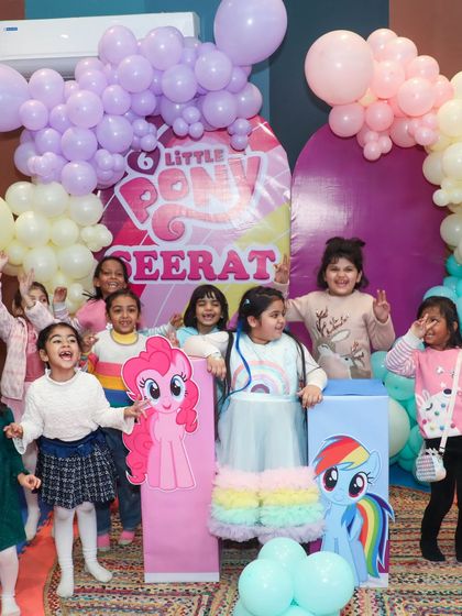 A group of happy kids posing with the birthday girl in front of the custom Little Pony backdrop.