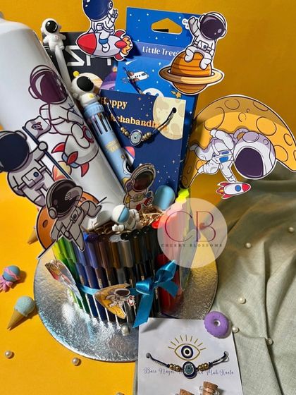 Our "To The Moon" Rakhi stationery hamper is a universe of fun. The colourful arrangement includes sketch pens, a diary, a sipper bottle, a keychain, and other space-themed goodies.