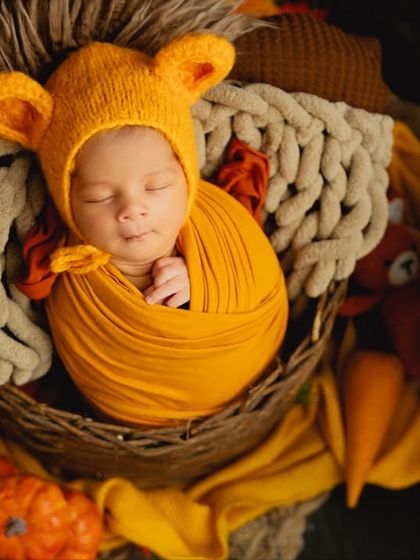 A close-up of a newborn in a bear bonnet, swaddled in orange and nestled in a basket, perfectly capturing the cozy feeling of an autumn-themed session.