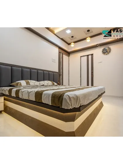 This bedroom in Bhiwandi has a clean, minimalist design with a dark upholstered headboard and a floating bed with under-lighting. The wardrobe doors feature alternating wood and laminate panels for a subtle decorative touch.