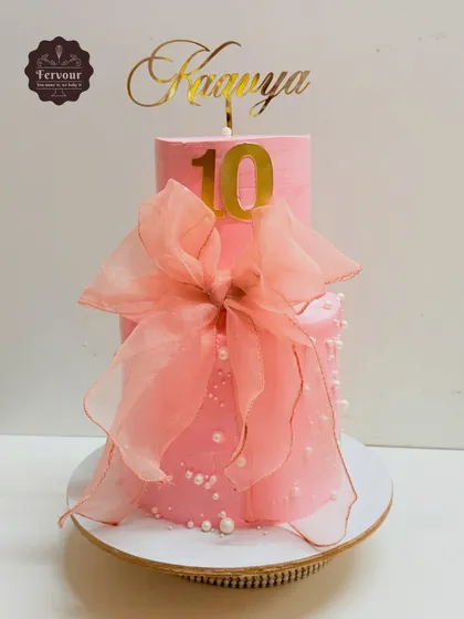A pretty pink two-tier cake for a 10th birthday. The design is simple and elegant, featuring a large, delicate organza bow and edible pearls.