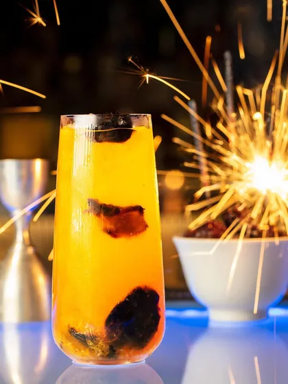 A festive cocktail shot for Hakkasan Mumbai, with a sparkler creating a celebratory feel. The bright sparks contrast beautifully with the dark background, highlighting the vibrant yellow drink.