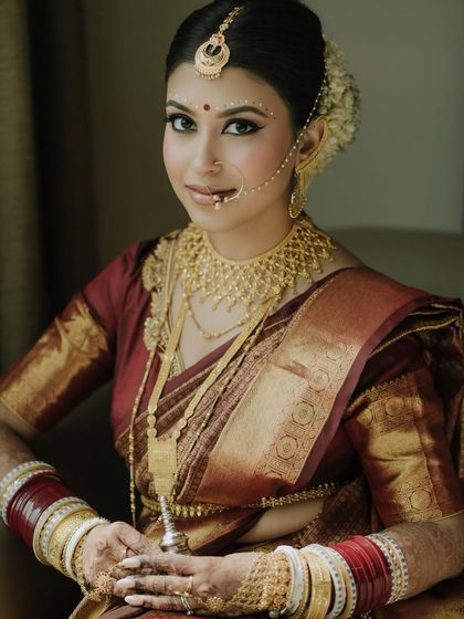 A full seated portrait showing the beautiful drape of the saree and the layers of traditional gold jewelry.