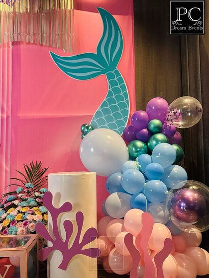 A detail shot of the mermaid party decor, highlighting the mermaid tail cutout and coral props. These elements, combined with the balloon clusters, are key to bringing the underwater theme to life.