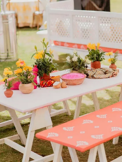 A picnic-style table setup for the 'Haldi Holi' event, complete with colorful florals and bowls of pink gulal.