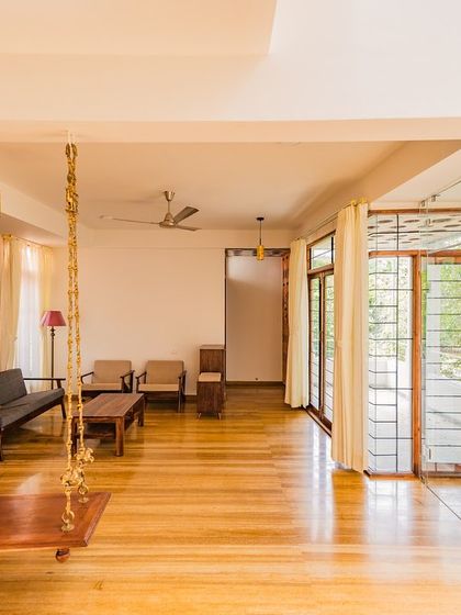 A wide view of the living area in the same home, showcasing the open layout and the traditional wooden swing. The space is designed to be flexible and airy, with large glass doors connecting to the outdoors.