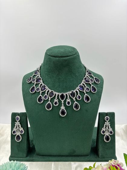 A contemporary silver-plated necklace set with teardrop-shaped stones. This design is available in emerald green, pink, red, and dark blue, offering a sleek and modern look for any occasion.