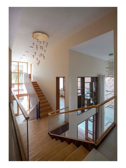 The multi-level staircase in the 'Pool Court House' wraps around the central void, offering constantly changing views of the pool and living areas. The use of wood and glass railings maintains a sense of lightness and transparency throughout the circulation path.