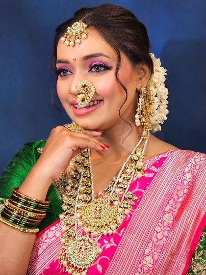 A smiling Maharashtrian bride in a pink and green saree. The makeup features a pop of pink on the eyes and lips for a fresh, celebratory look.
