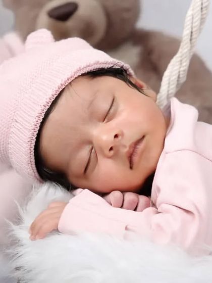 A close-up of a newborn in a pink bear-eared hat, sleeping soundly next to soft teddy bears. This shot focuses on the peaceful and adorable details.