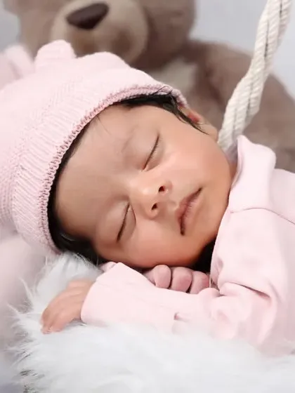 A close-up of a baby in a pink bear-ear hat, sleeping peacefully among soft teddy bears.