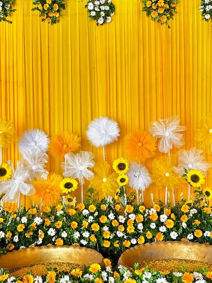 A cheerful Haldi backdrop combining a solid yellow drape with a mix of real sunflowers, white and yellow daisies, and delicate paper flowers.