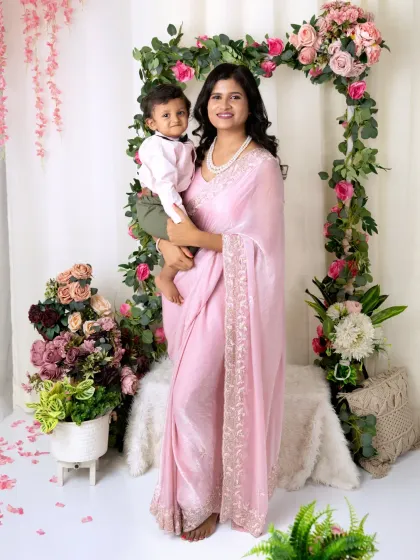 A mother in a beautiful pink saree stands and holds her son, creating an elegant and loving portrait.