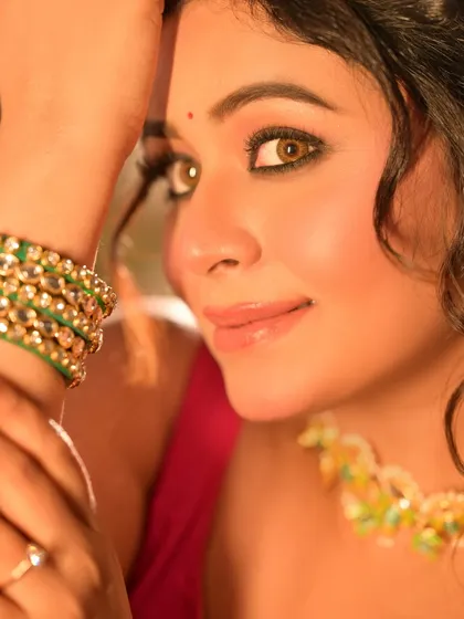 A close-up on the model's face, highlighting her sparkling eyes and traditional green bangles. The warm lighting gives her skin a beautiful glow.